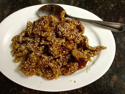 Sesame Beef: breaded, deep fried cuts of beef stir fried in a tangy, dark orange sauce garnished with sesame seeds.