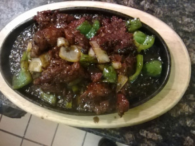 Sizzling Beef with Black Pepper Sauce: cuts of beef stir fried with green peppers and white onions in a black bean sauce, served on a sizzling hot cast iron plate.